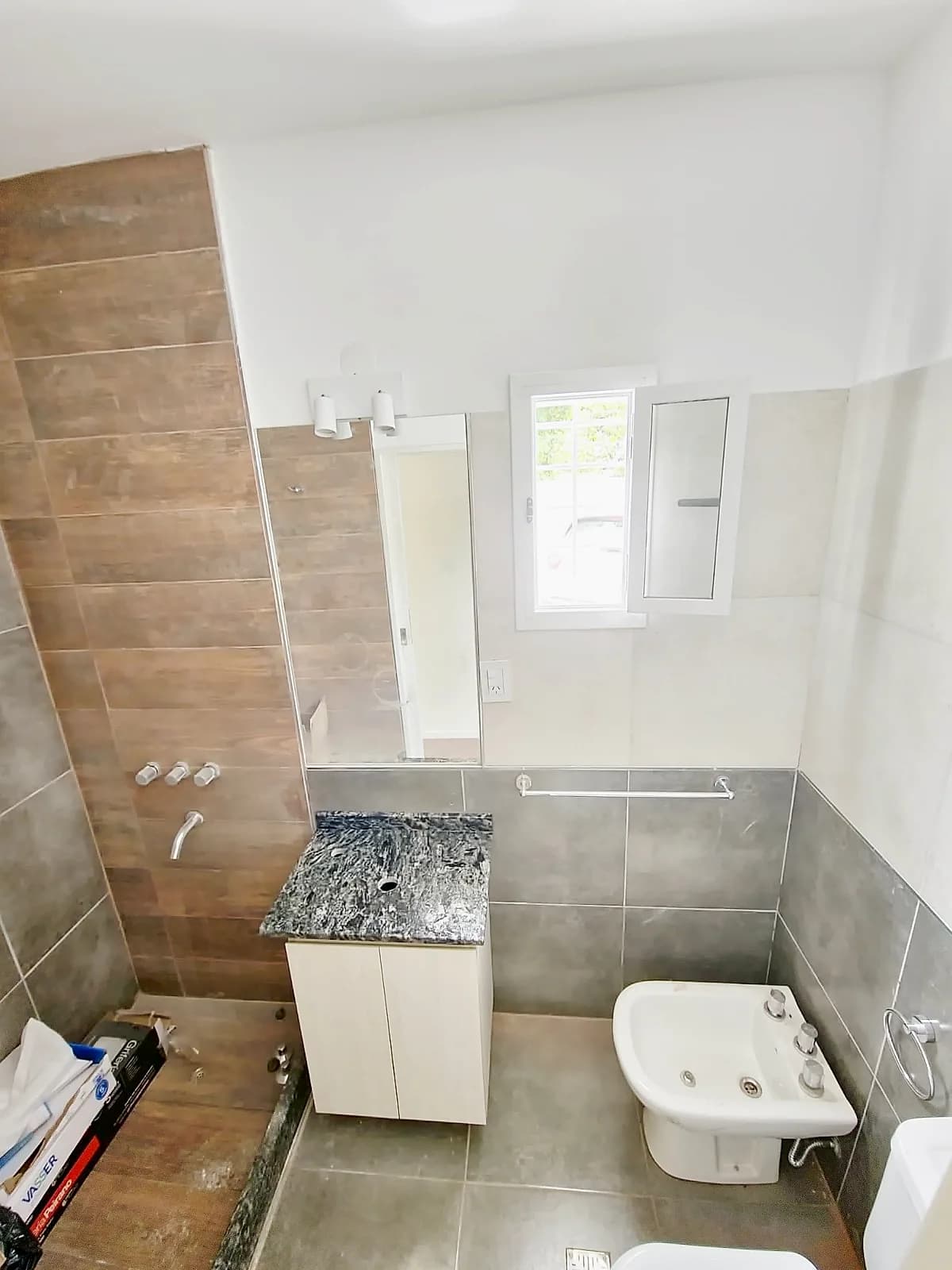 Baño con sector de ducha revestido, mueble de guardado y mesada de granito