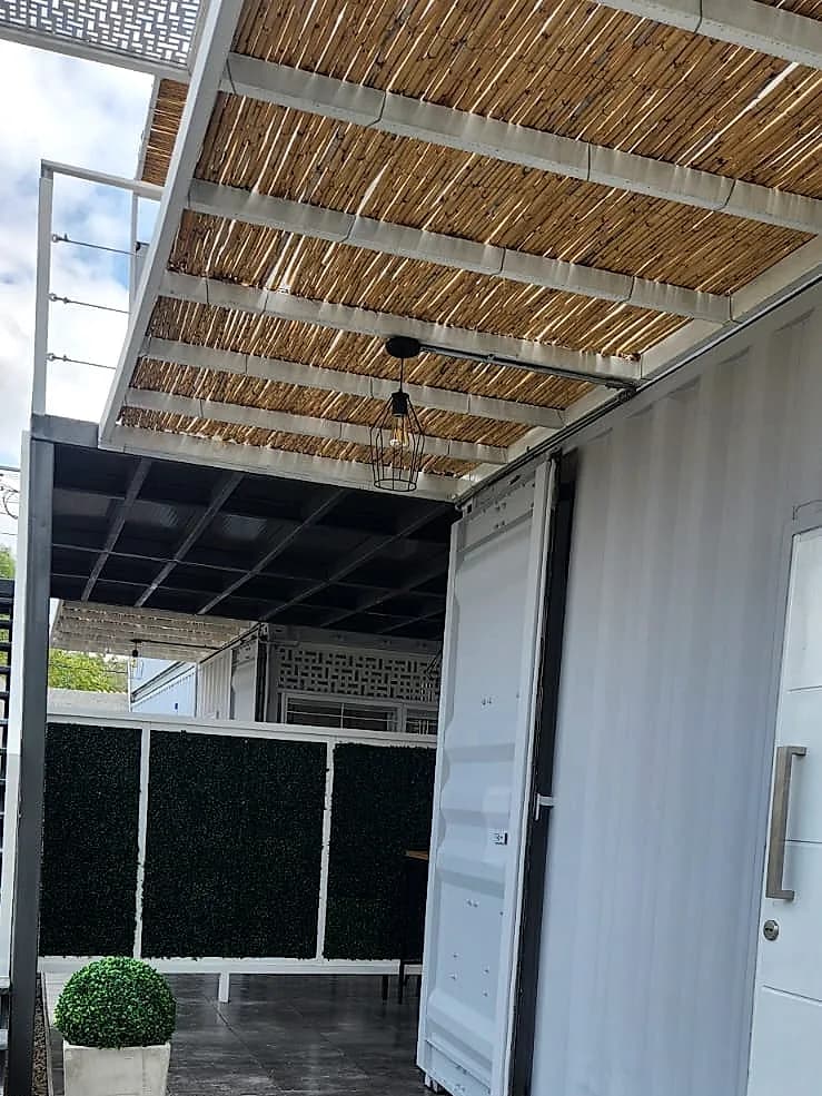 Galería exterior del Eco Home con pérgola de madera, piso cerámico y acceso independiente